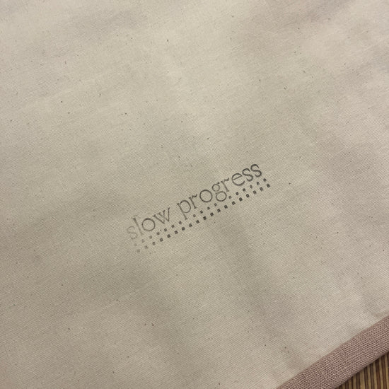 Beige linen with stone coloured trim back of quilted wall hanging with slow progress logo stamped in black