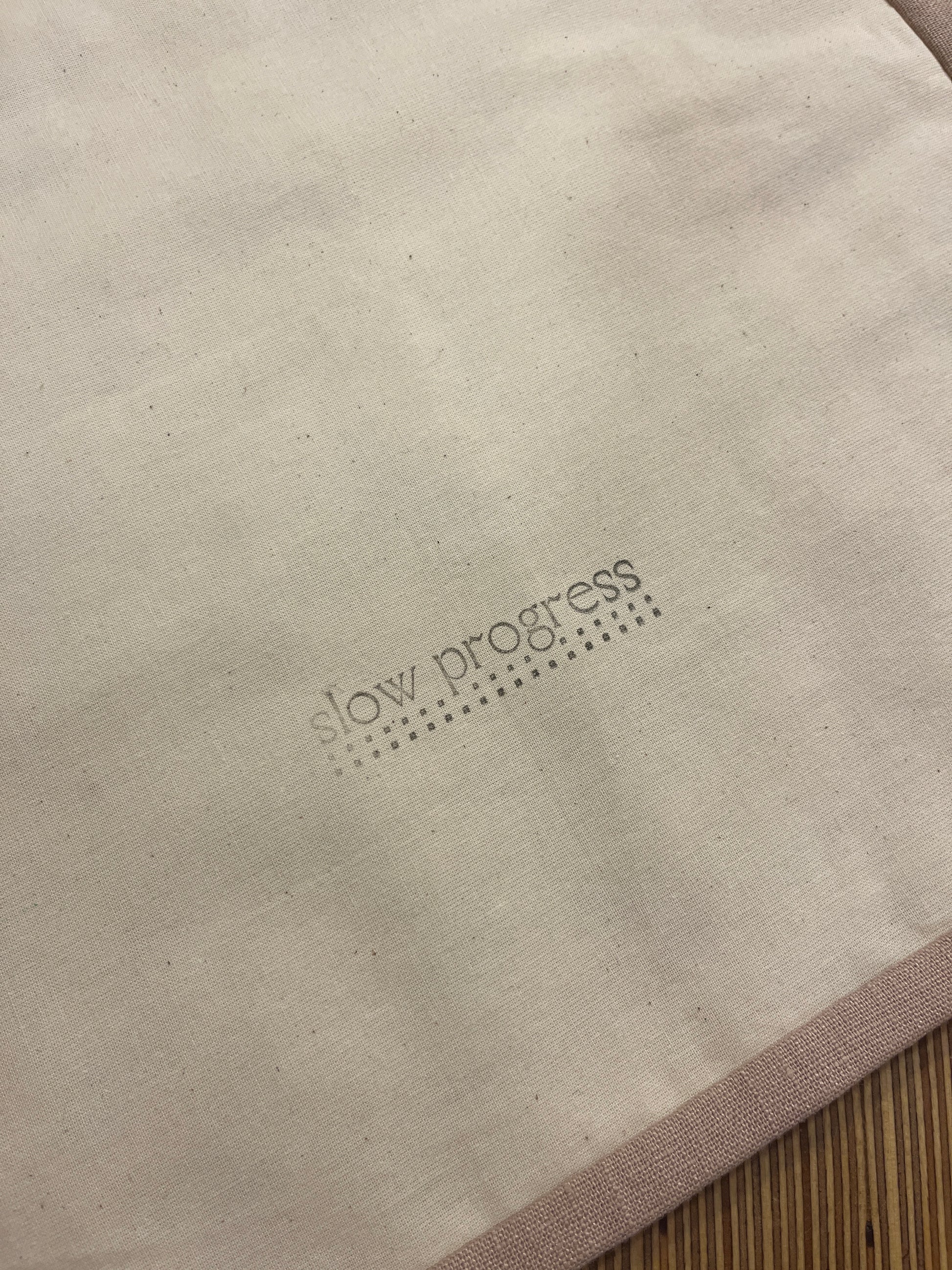 Beige linen with stone coloured trim back of quilted wall hanging with slow progress logo stamped in black