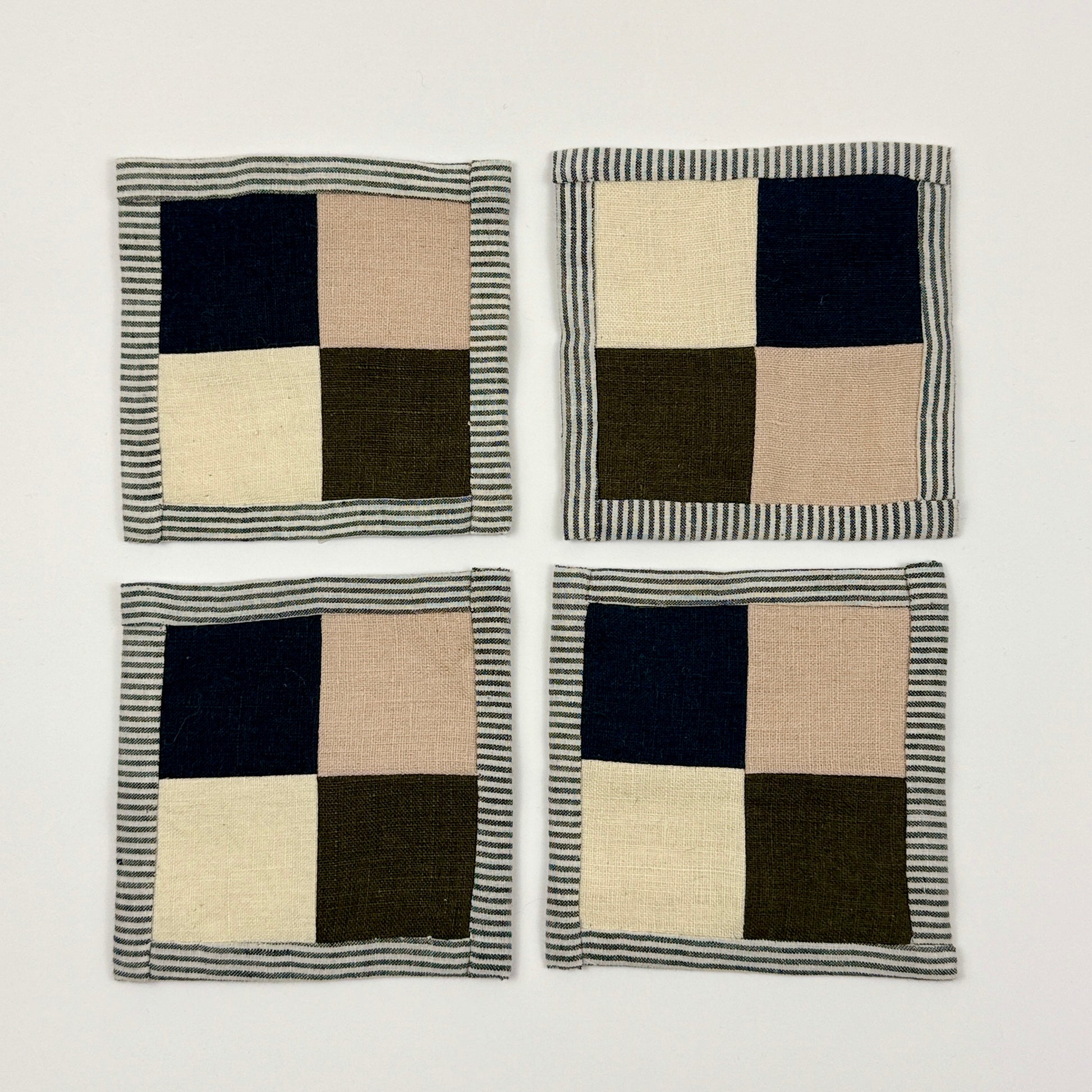 Four checkered coasters with navy, beige, and green squares on a white background