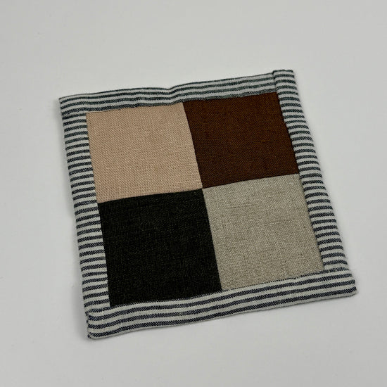 Square linen patchwork coaster with a striped border on a light gray background