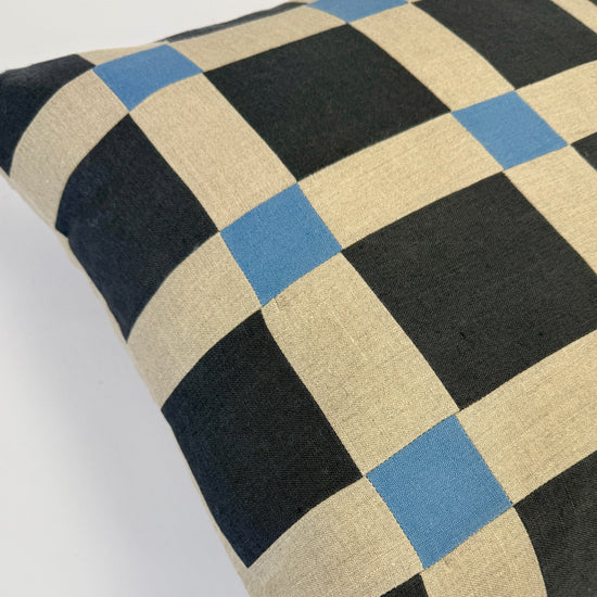 Checkered pillow with black, beige, and blue squares on a white background