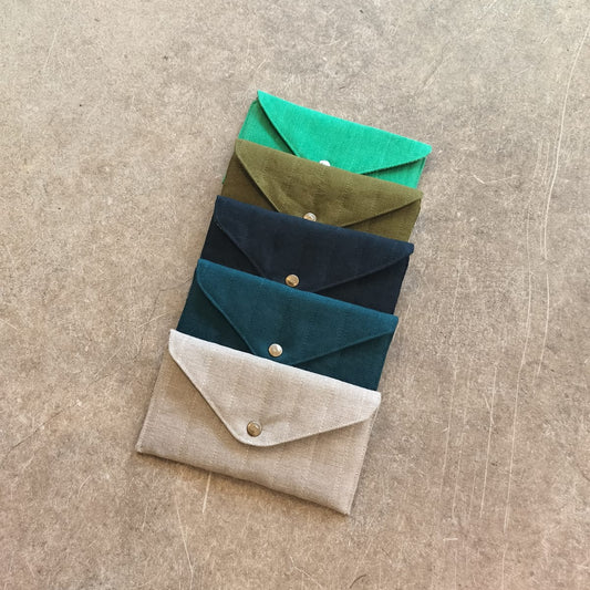 A collection of quilted pouches in beige, green, blue, and brown colors, arranged one inside the other on a textured background.