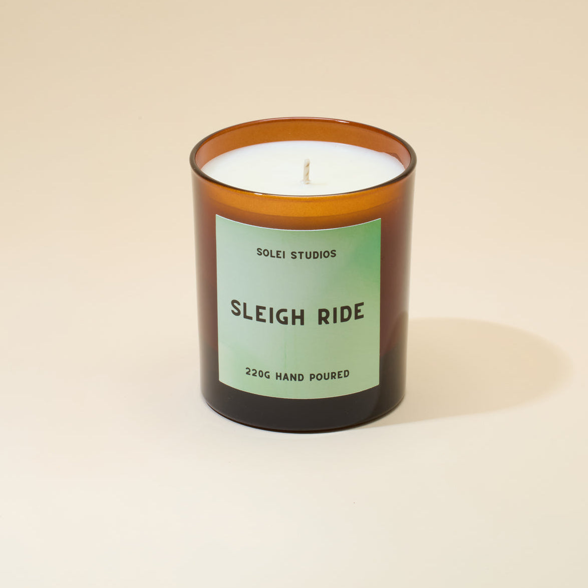 A candle jar with a green label on a soft peach background