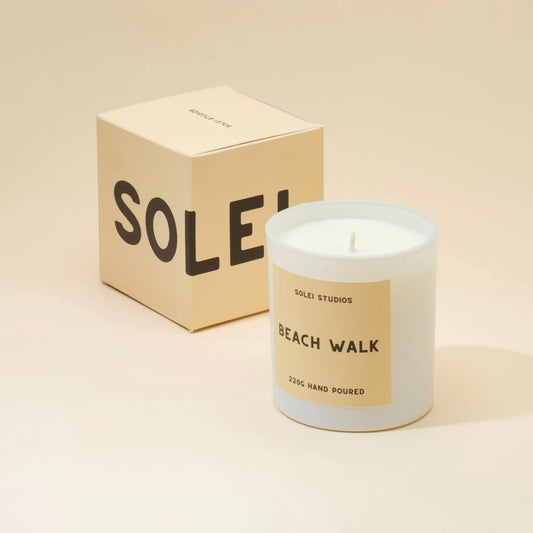Candle labeled 'Beach Walk' by SOLEI STUDIOS with packaging on a beige background