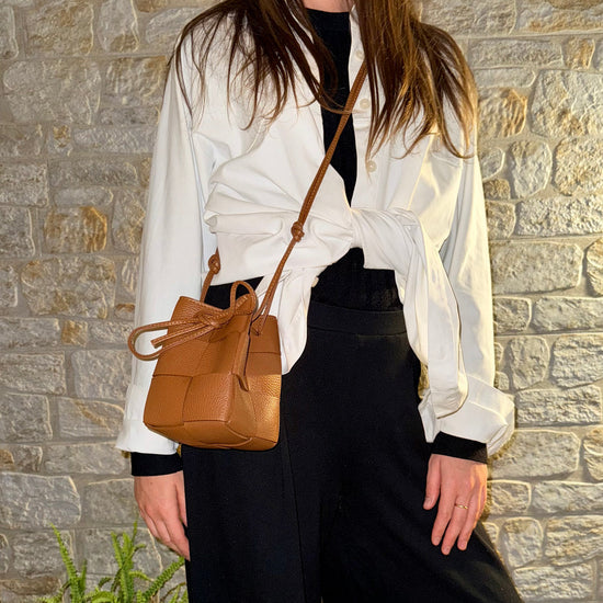 A woman wearing a black and white outfit on a stone background with a brown handbag