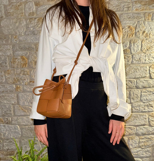 A woman wearing a black and white outfit on a stone background with a brown handbag
