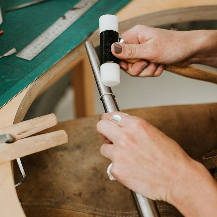 Person using a tool on a leather item with a workbench in the background
