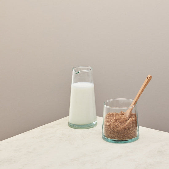 A jug of milk and a small jug of sugar on a taupe background 