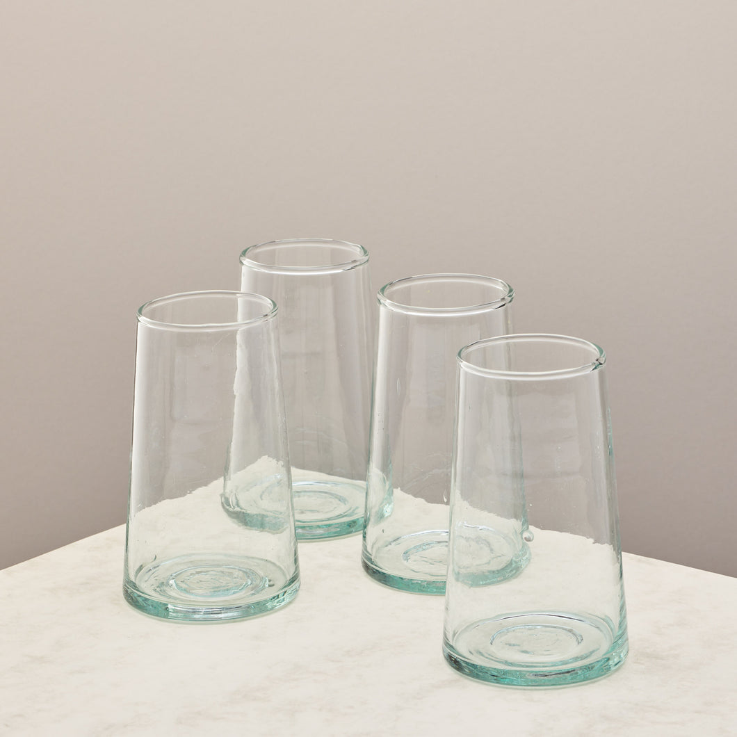 Four clear glass tumblers on a white surface with a beige background