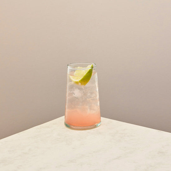 Glass of pink cocktail with a lime wedge on a beige surface and background