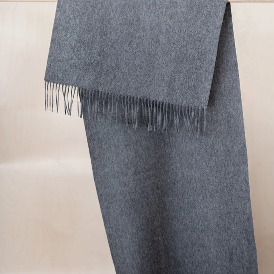 A folded grey woolen scarf with fringed edges, displayed against a light beige background.