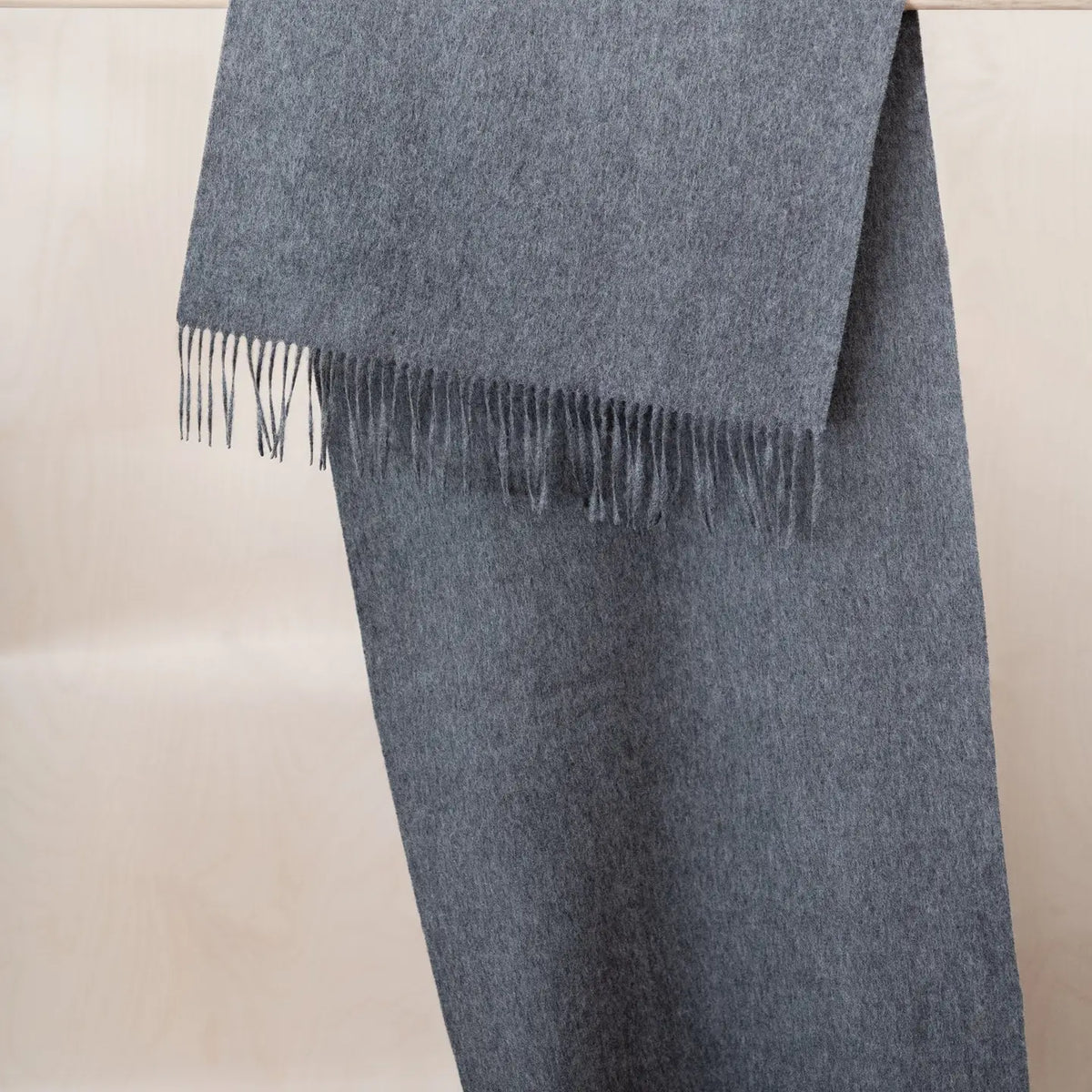 A folded grey woolen scarf with fringed edges, displayed against a light beige background.
