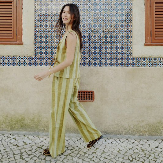 Woman in a striped green and brown outfit standing in front of a patterned wall.