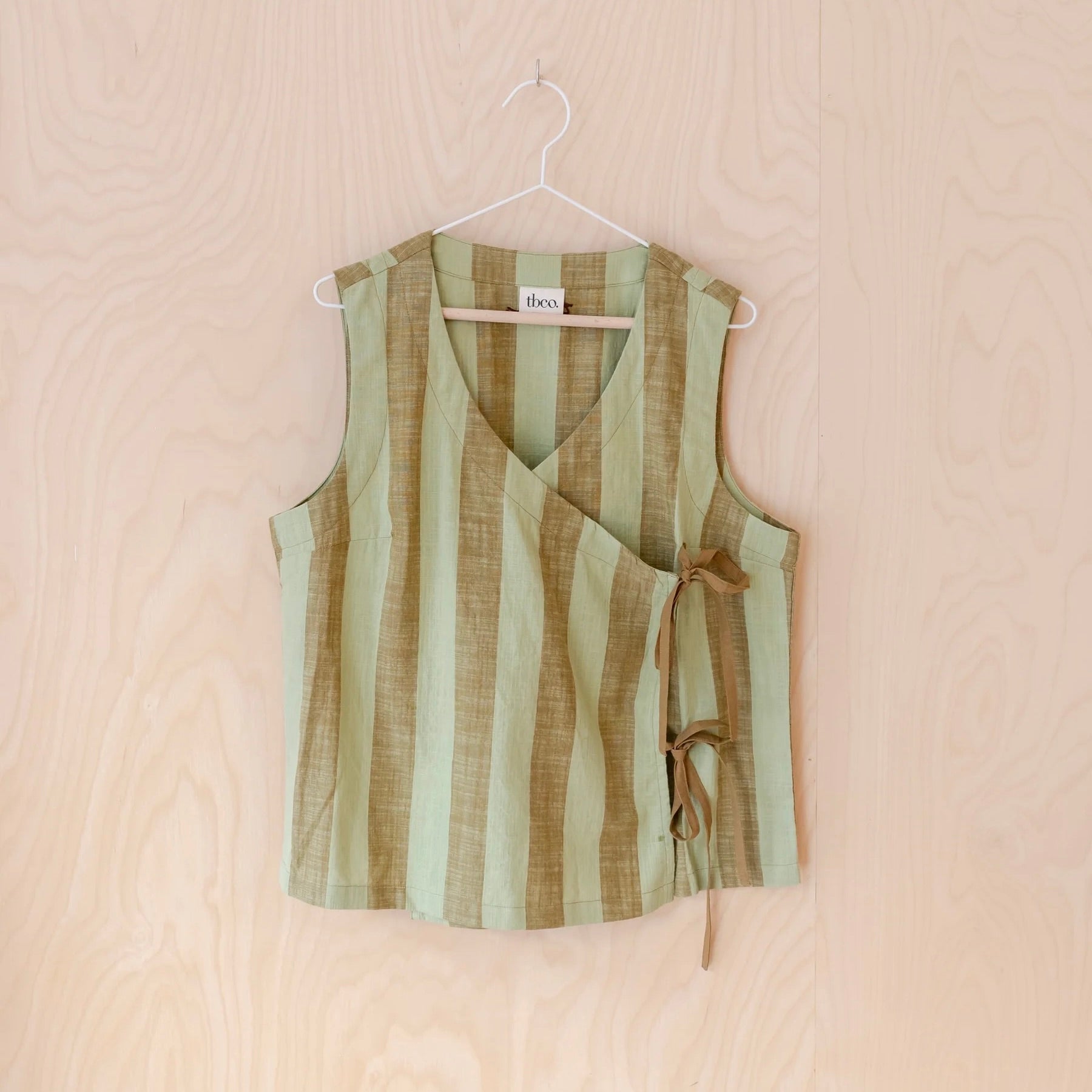 Green and brown striped sleeveless tie top on a hanger against a beige background