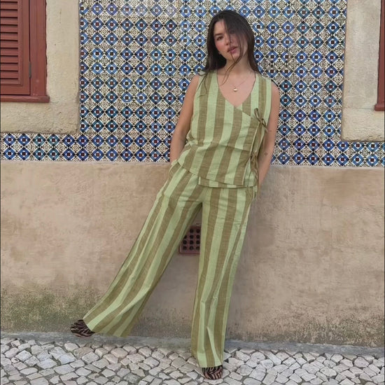 Woman in a green and brown striped outfit standing against a patterned wall.