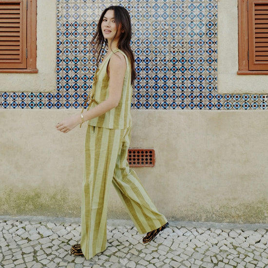 Woman in a striped green and brown  outfit standing in front of a patterned wall.