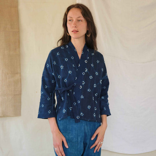 Woman wearing a navy blue patterned top and jeans against a neutral background
