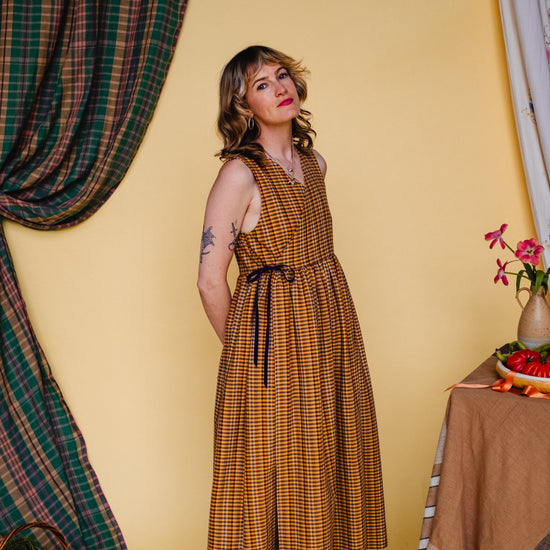 Woman in a checkered dress standing against a yellow wall with decorative elements.