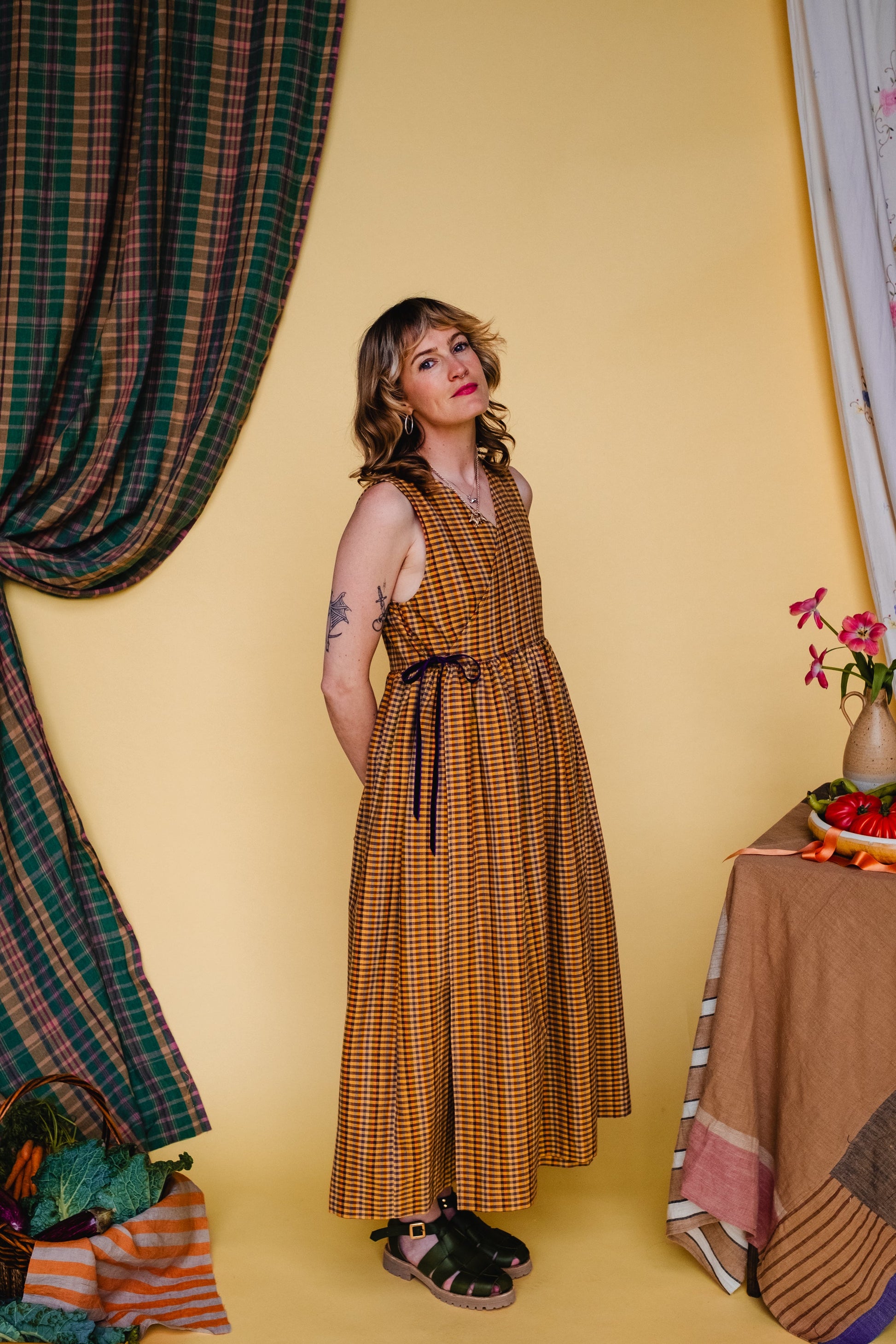 Woman in a checkered dress standing against a yellow wall with decorative elements.