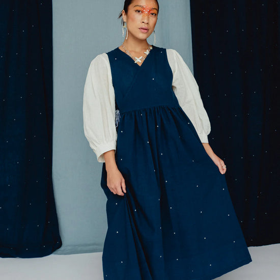 Woman wearing a navy dress with white embroidered posies against a blue background