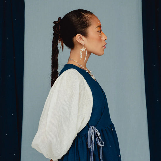 Woman wearing a blue dress with white embroidered posies with a white blouse against a blue background