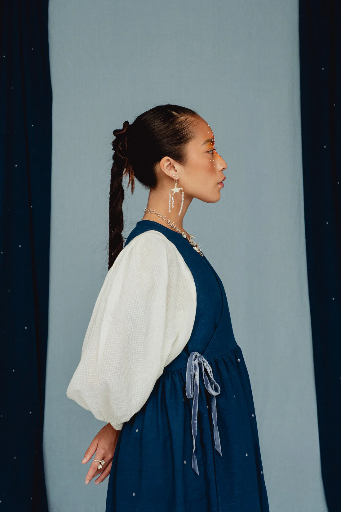 Woman wearing a blue dress with white embroidered posies with a white blouse against a blue background