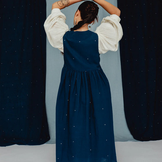 Person wearing a blue dress with white embroidered posies against a blue backdrop