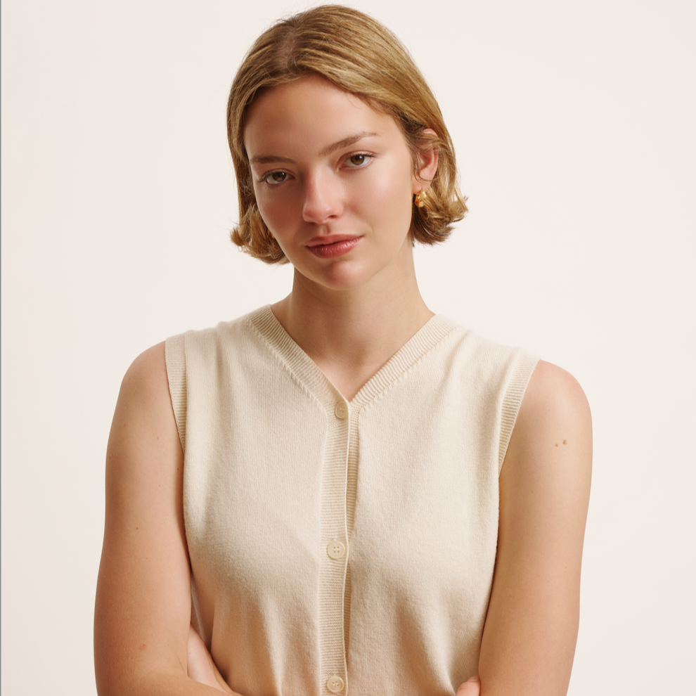 Woman wearing a beige sleeveless cardigan against a plain background