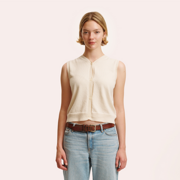 Woman wearing a beige sleeveless top and light blue jeans on a plain background