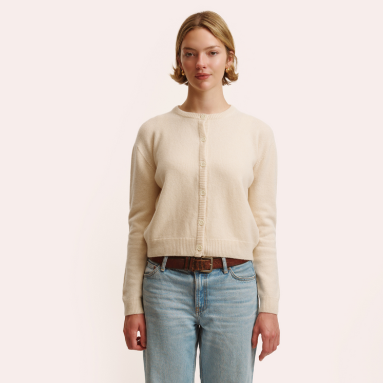 Woman wearing a beige cardigan and light blue jeans on a plain background