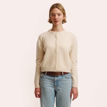 Woman wearing a beige cardigan and light blue jeans on a plain background