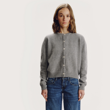 Woman with blonde hair wearing grey wool knitted long sleeves round neck cardigan with front centre white button fastenings on a grey background