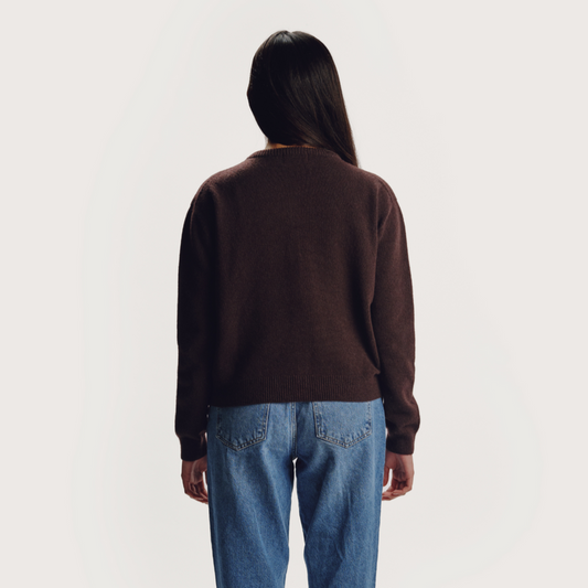 Person wearing a brown sweater and blue jeans on a white background