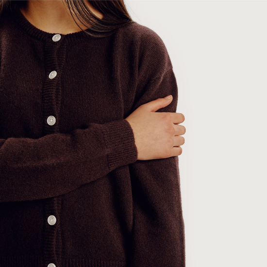 Brown cardigan with button details worn by a person on a white background