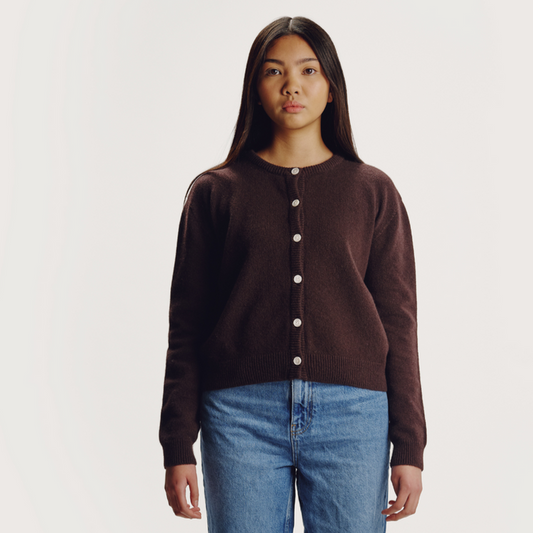 Woman with long brown hair wearing brown wool knitted long sleeves round neck cardigan with front centre white button fastenings on a grey background