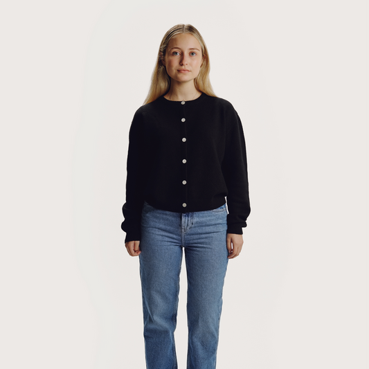 Woman with long blonde hair wearing black wool knitted ling sleeves round neck cardigan with front centre white button fastenings on a grey background