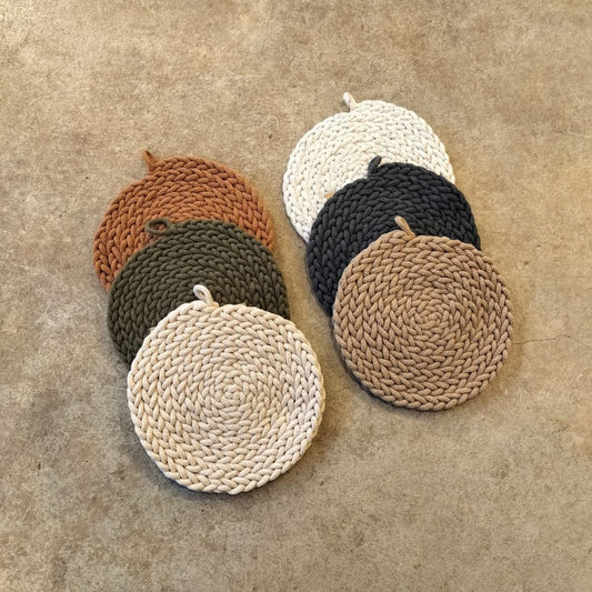 A collection of round rope trivets in various colors placed on a textured surface.