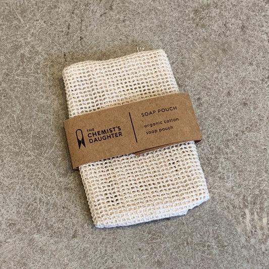 A white cotton soap pouch with a norwich business card showing 'The Chemist's Daughter' branding on it, placed on a textured surface.