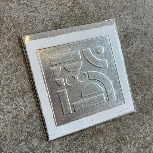 Silver leaf embossed geometric abstract print with a white boarder on heritage cotton paper. Square shaped on a grey concrete background