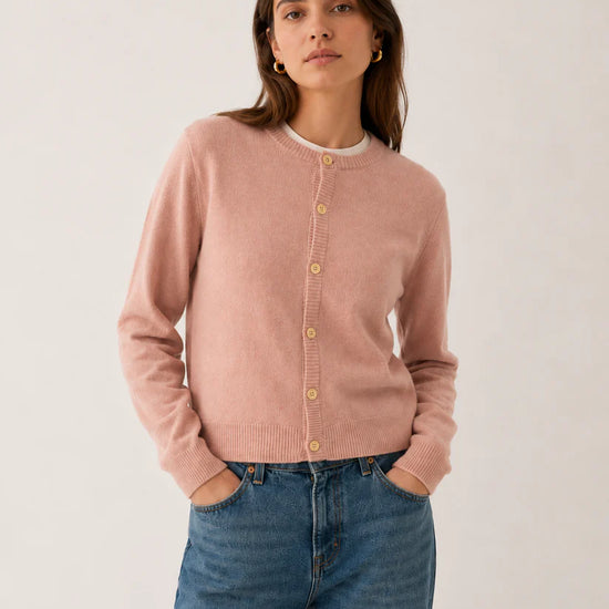 Woman wearing a pink lambswool cardigan and blue jeans against a white background