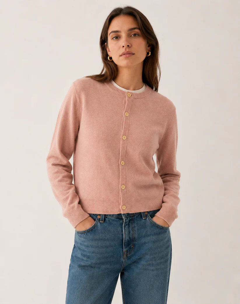 Woman wearing a pink lambswool cardigan and blue jeans against a white background