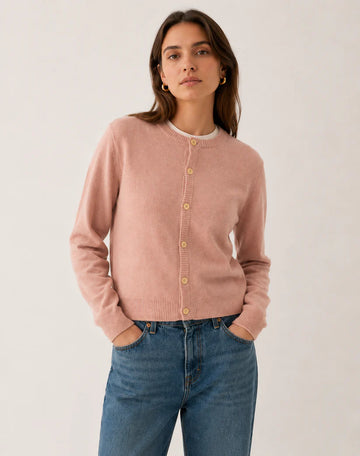 Woman wearing a pink lambswool cardigan and blue jeans against a white background