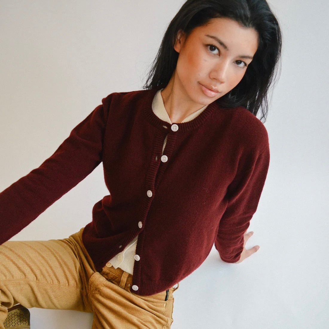 Woman wearing a port cardigan with white buttons on a plain background