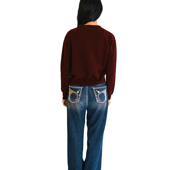 Person wearing a port sweater and blue jeans with decorative back pockets on a white background