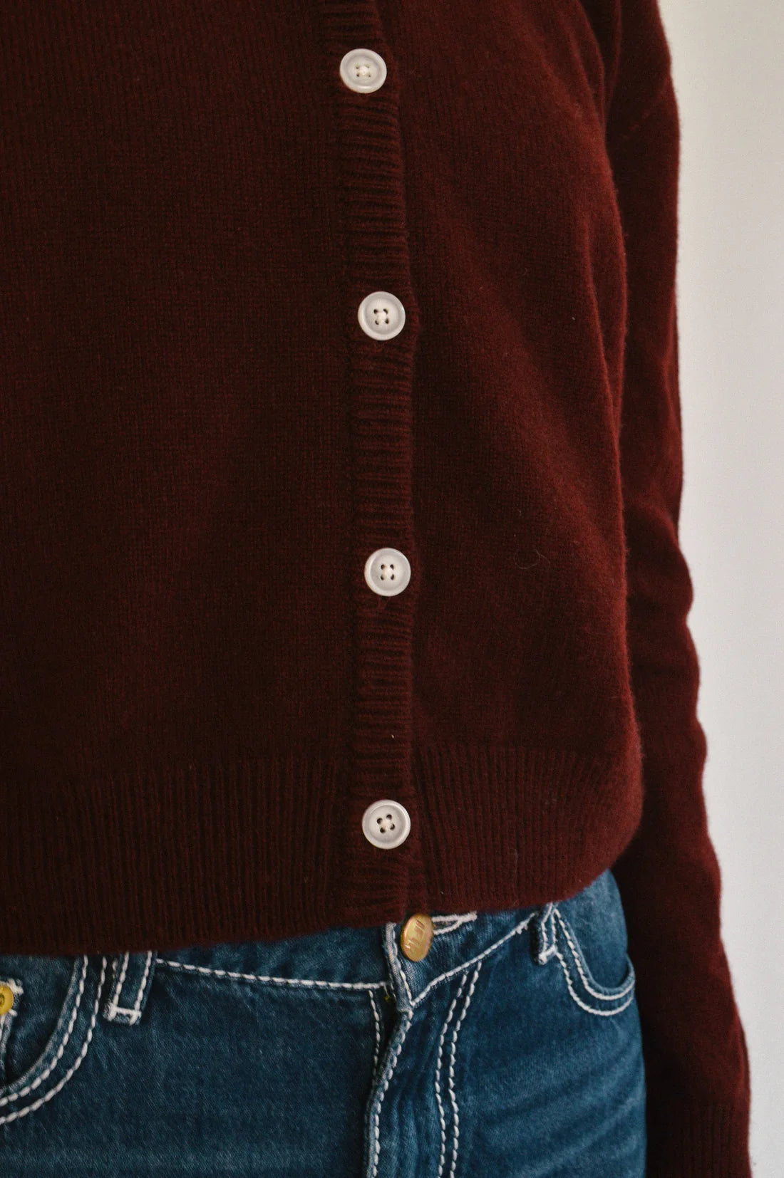 Close-up of a port button-up cardigan worn over blue jeans on a white background