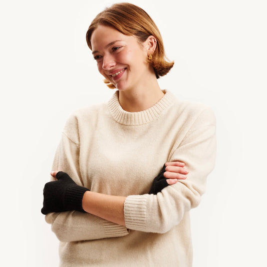 Woman wearing a beige sweater and black gloves on a white background