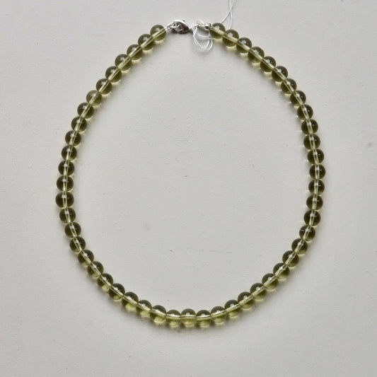 A beaded necklace made of translucent olive-green gemstone beads, arranged in a circle on a light gray background. It features a silver clasp at the top.