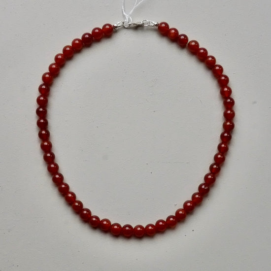 A beaded necklace made of round, polished red gemstone beads with a silver clasp, displayed on a light gray background.