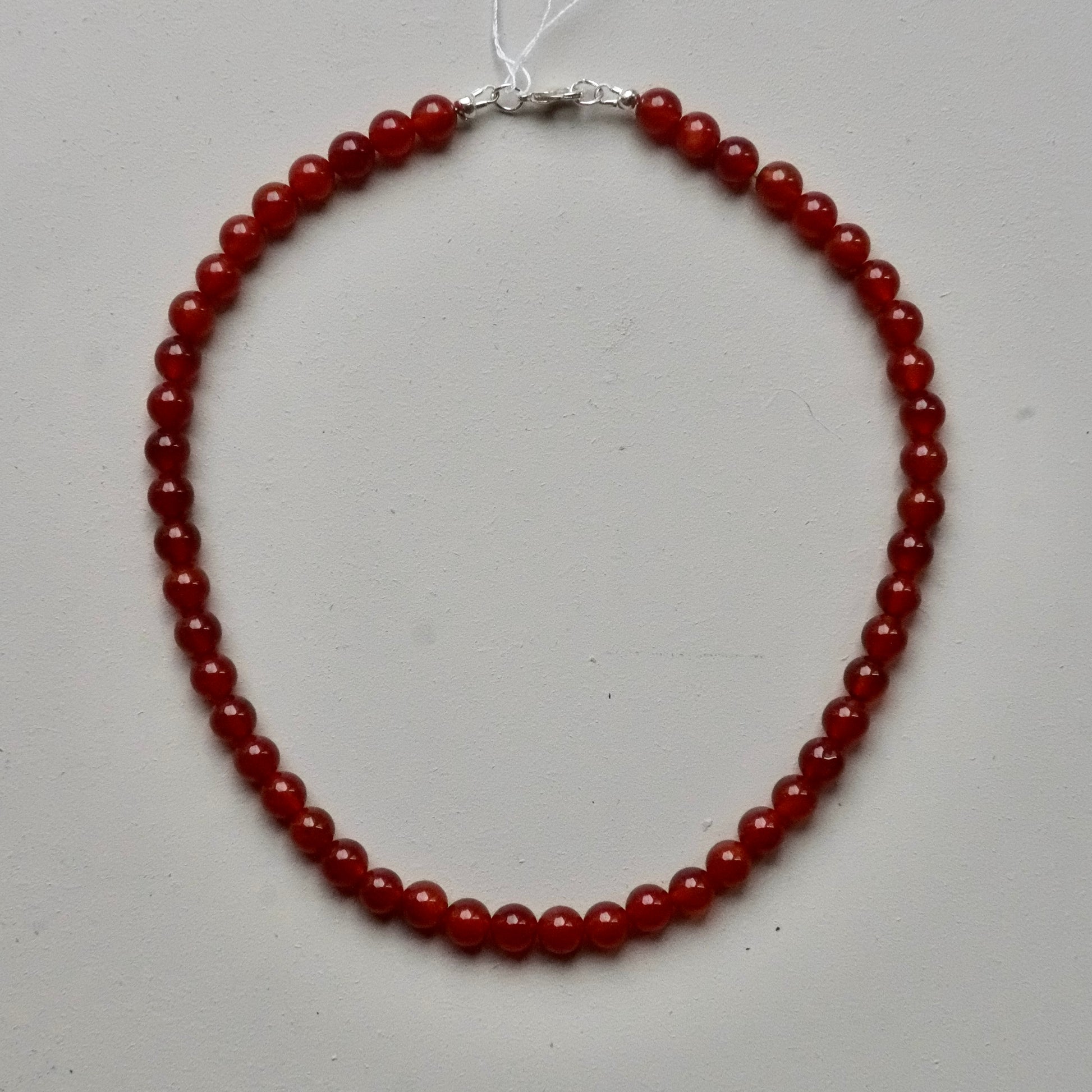 A beaded necklace made of round, polished red gemstone beads with a silver clasp, displayed on a light gray background.