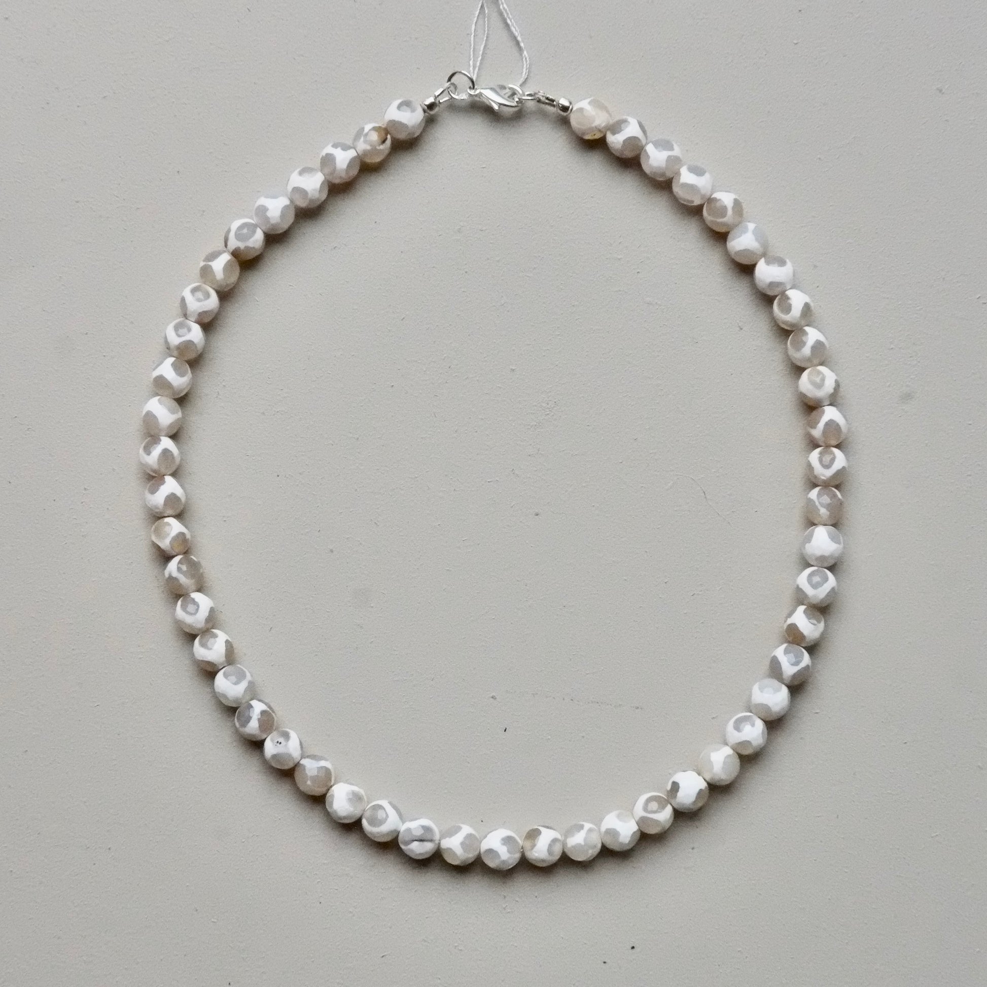 A single-strand necklace made of irregular, faceted white shell beads, displayed on a neutral light gray background.